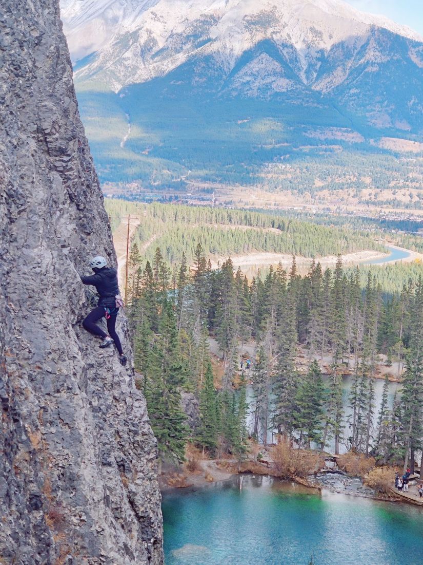 A climber partway up a rock face above a green lake