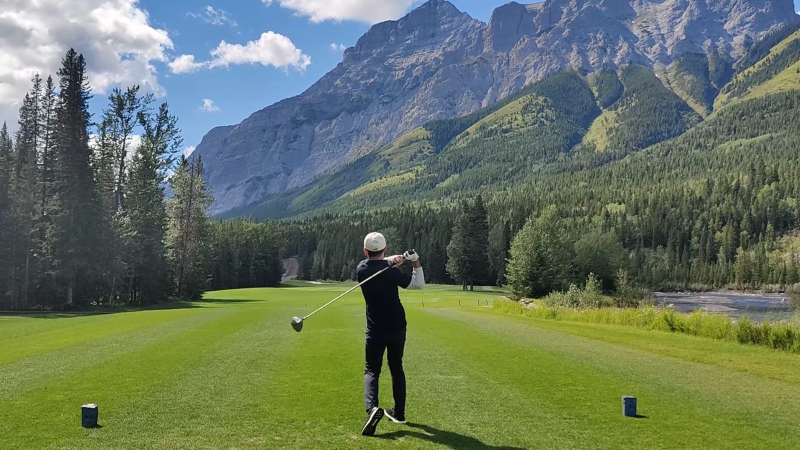 A golfer at the top of the follow-through on a fairway below a mountain wall