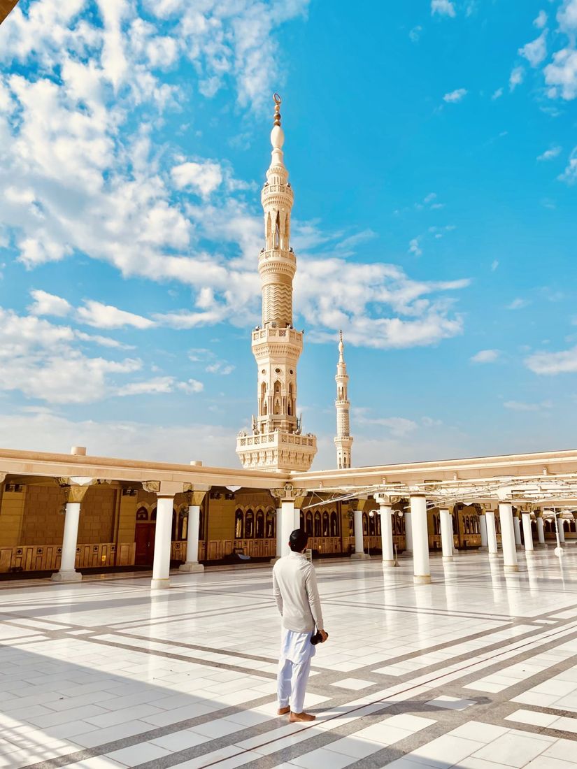 A figure standing on a marble courtyard beneath a tall minaret